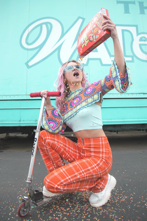 Model Libby Morgan wears bold pants, a teal crop top and crochet over-layer while showering herself in Fruit Loops for an epic action shot