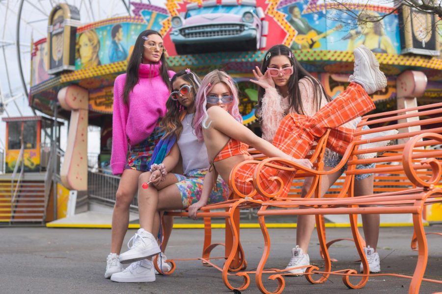 Models Emma Bowder, Amneet Singh, Libby Morgan and Natalie Cornejo pose on a amusement park bench showing off their 90s inspired looks.
