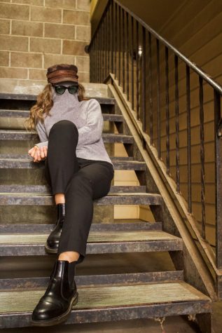 Jessica Thompson, sits on staircase with her sweater and glasses covering her face.