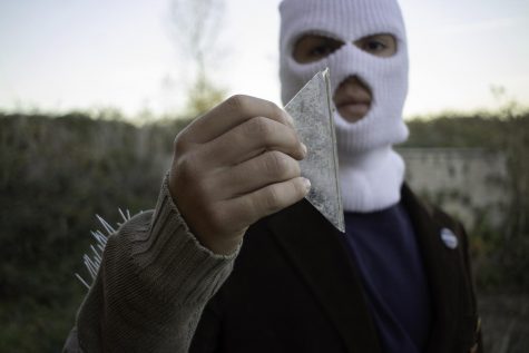 Model Jayson Hwathrone wears white ski masks and holds a piece of broken glass